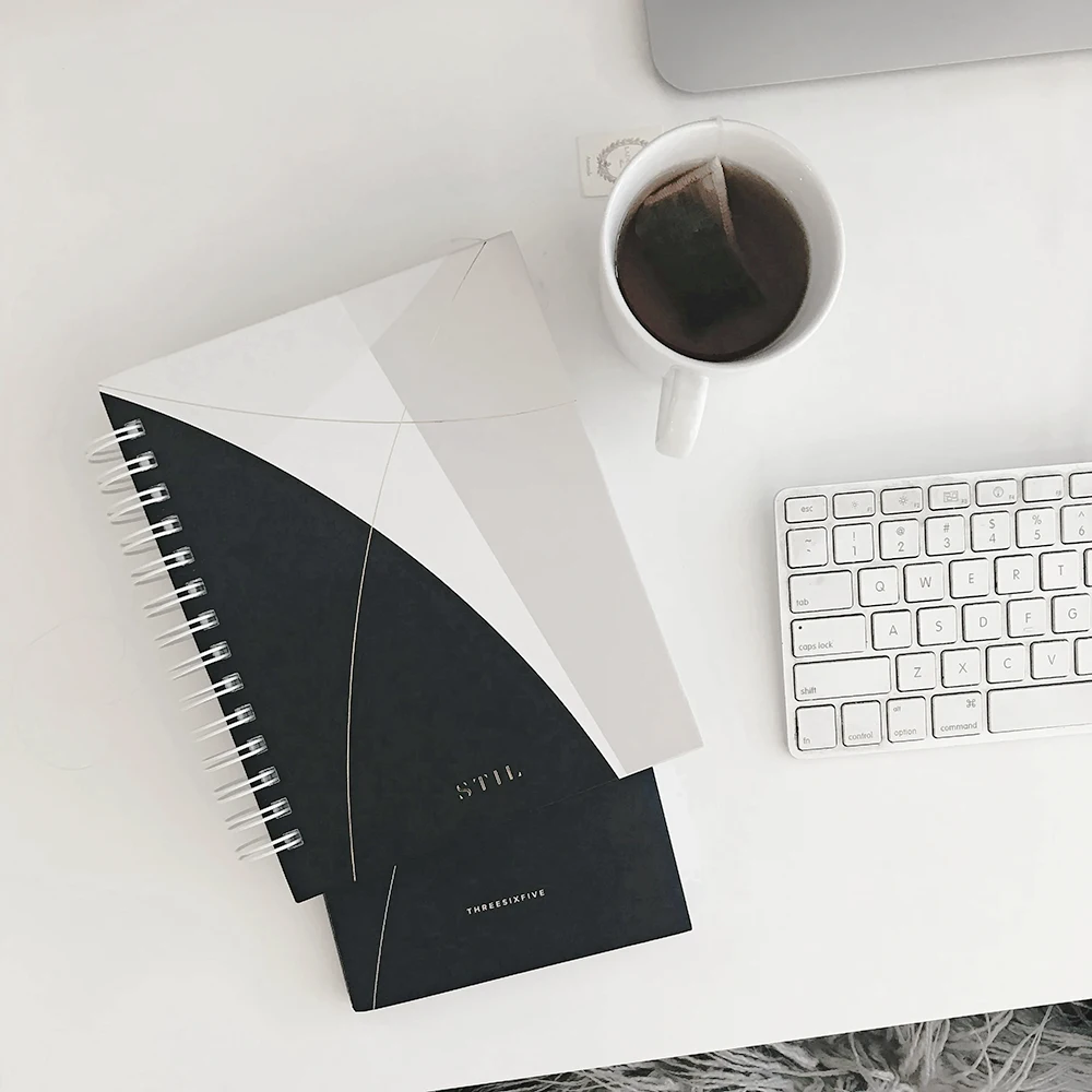 Notizbuch, Tee und Tastatur auf weißem Tisch – Symbolbild für Kommunikationskonzept und Strategie: Klarheit, Struktur, Fokus.