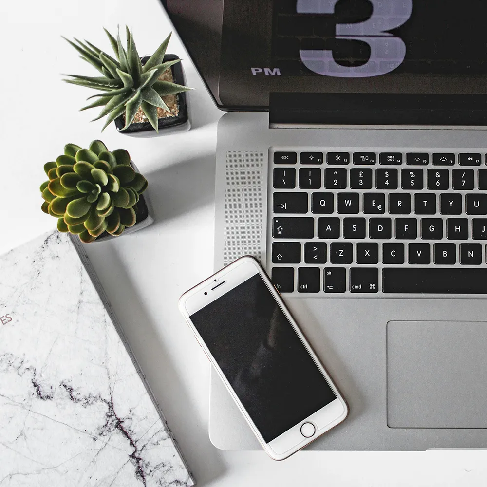 Laptop mit iPhone und 3-PM-Uhr – Symbolbild für Social-Media-Management: Planung, Gestaltung, Steuerung.